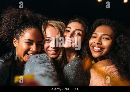 Gruppenporträt von vier glücklichen Freundinnen, die nachts Kopf an Kopf im Freien stehen Stockfoto