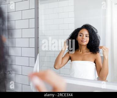 Eine wunderschöne Frau, die nach dem Duschen in ein weißes Handtuch gewickelt war und ihr Spiegelbild anschaute Stockfoto