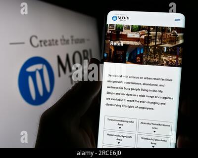 Person, die ein Mobiltelefon mit einer Webseite des japanischen Immobilienunternehmens Mori Trust Co. Ltd. Auf dem Bildschirm mit Logo hält. Konzentrieren Sie sich auf die Mitte des Telefondisplays. Stockfoto