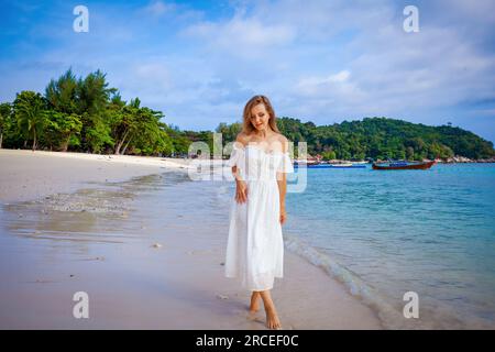 Eine Frau in weißem Kleid geht mit Muscheln am tropischen Strand spazieren Stockfoto