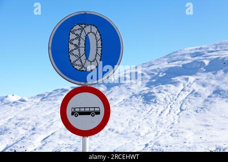 Ein Schild mit Schneeketten ist erforderlich über einem Busverbot-Schild vor einem schneebedeckten Berg in den Pyrenäen. Stockfoto