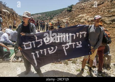 Salfit, Palästina. 14. Juli 2023. Israelische linke Aktivisten halten während ihrer Demonstration mit palästinensischen Demonstranten gegen die illegale Errichtung jüdischer Siedlungen auf palästinensischem Boden im Dorf Deir Istiya, westlich des Gouvernements Salfit, ein Banner mit Slogans. Kredit: SOPA Images Limited/Alamy Live News Stockfoto