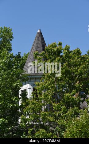 Altes, historisches, viktorianisches Haus wurde überwuchert und verlassen. Der runde Turm ist mit einer Zinnkappe und Schindeln gekrönt. Die Farbe ist rissig und blättert ab. Stockfoto