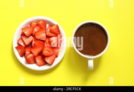 Eine Tasse Kaffee und gehackte Erdbeeren auf einem Teller mit gelbem Hintergrund, Draufsicht, flach liegend. Frische Erdbeeren. Platz kopieren, für Text platzieren. Bref Stockfoto