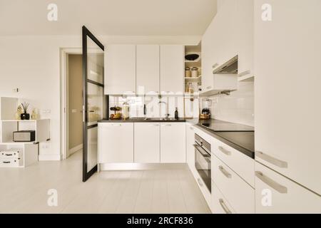 Eine moderne Küche mit weißen Schränken und schwarzen Ablageflächen auf der Insel in diesem kleinen Raum ist sehr gut organisiert Stockfoto