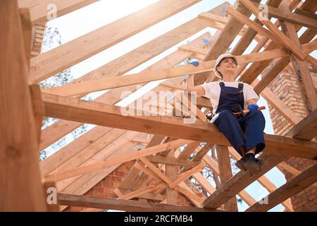 Eine Frau, die Hammer hält, sich von der Decke ruht, auf dem Dachträger sitzt Stockfoto