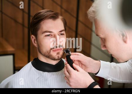 Ein gutaussehender Mann, der vom Friseur in einem modernen Friseursalon bedient wird Stockfoto