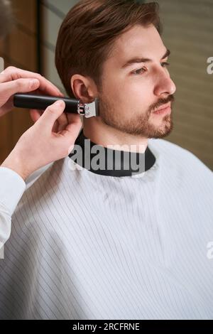 Ein gutaussehender Mann, der vom Friseur in einem modernen Friseursalon bedient wird Stockfoto