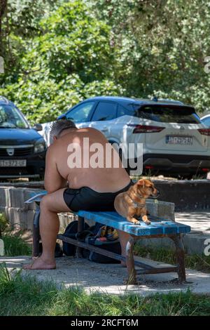 Großer älterer Mann, der mit seinem Hund auf einer Bank sitzt, Mann mit Hund, ein Mann und sein Hund, bester Freund des mannes, Mann und Hund, der in der Sonne auf der Bank sitzt. Stockfoto