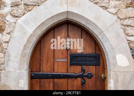 Große Bogentür aus Holz mit Eisenband-Scharnieren im mittelalterlichen Stil, Steinbogen, der die Tür zu dicker Eiche umgibt. Briefkasten und Türklopfer an schwerer Tür. Stockfoto