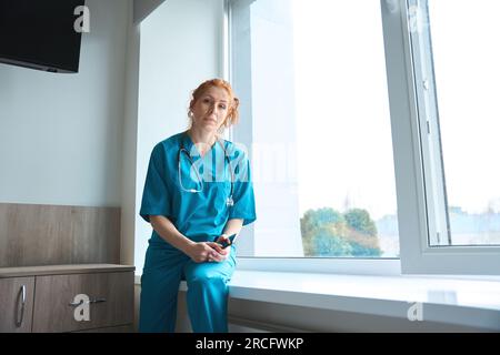 Ärztin, die im Krankenhaus auf der Fensterbank sitzt Stockfoto