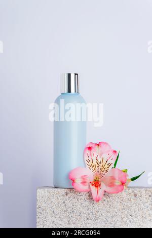 Kosmetik-Gesichtsreiniger-Flasche und Alstroemeria-Rosa-Blume auf Natursteinpodium, Nahaufnahme. Stockfoto