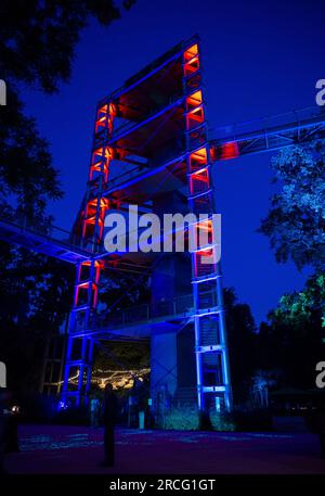 Beelitz, Deutschland. 14. Juli 2023. Der Aussichtsturm auf dem Gelände des Baumwipfels „Baum & Zeit“ in Beelitz-Heilstätten ist abends rot beleuchtet. An drei Abenden im Juli und August bietet der Abenteuerbereich seinen Gästen ein Abendprogramm mit Musik, Lichtinstallationen und Vorstellungen. Kredit: Monika Skolimowska/dpa/ZB/dpa/Alamy Live News Stockfoto