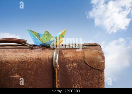 Papierboot gefaltet von einer Karte auf einem alten alten Koffer vor einem blauen Himmel mit weißen Wolken, Wanderlust, Kreuzfahrt- und Reisekonzept, Kopierraum, SELEC Stockfoto