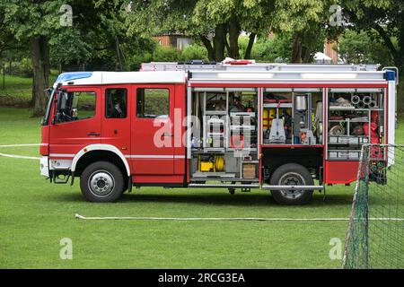 Deutsches Feuerwehrauto, roter Lastwagen mit offenen Rollladentüren und die Ausrüstung für die Brandbekämpfung, auf einer Wiese während einer Übung, Kopierraum Stockfoto