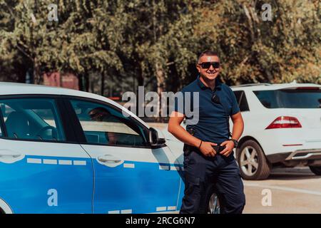 Ein Polizist patrouilliert in der Stadt. Ein Polizist mit Sonnenbrille patrouilliert in der Stadt mit einem offiziellen Polizeiauto Stockfoto