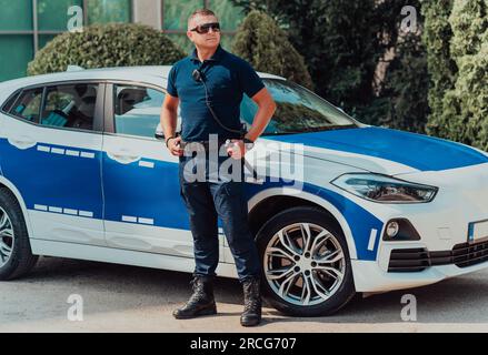 Ein Polizist patrouilliert in der Stadt. Ein Polizist mit Sonnenbrille patrouilliert in der Stadt mit einem offiziellen Polizeiauto Stockfoto
