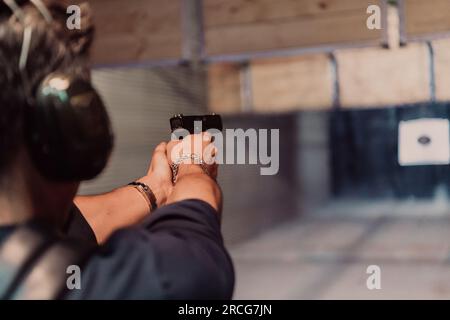 Ein Mann übt das Schießen mit einer Pistole auf einem Schießstand, während er schützende Kopfhörer trägt Stockfoto
