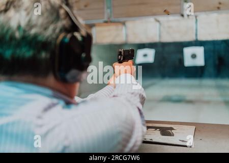 Ein Mann übt das Schießen mit einer Pistole auf einem Schießstand, während er schützende Kopfhörer trägt Stockfoto