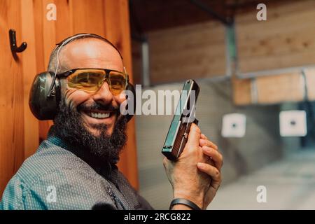 Ein Mann übt das Schießen mit einer Pistole auf einem Schießstand, während er schützende Kopfhörer trägt Stockfoto