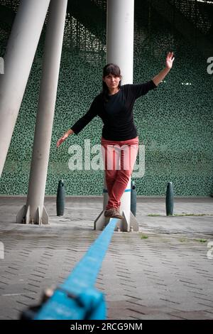 Eine peruanische Frau mit roten Hosen und schwarzem T-Shirt läuft auf einem Blauen Seil und praktiziert Slack Line Stockfoto