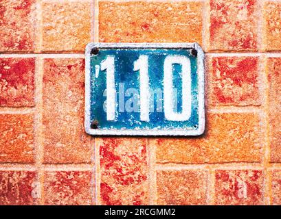 Nummer 110, 1010, blau auf rotem Ziegelstein. Stockfoto