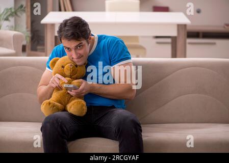 Junger Mann, der zu Hause mit Bärenspielzeug sitzt Stockfoto