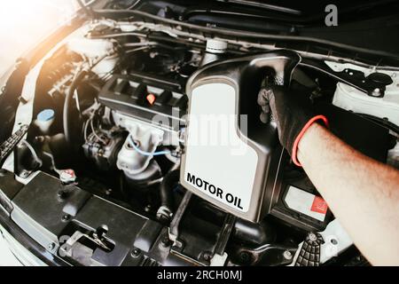 Hand eines Mechanikers, der eine Flasche Motoröl im Motorraum eines Autos hält, Schmiermittelwechsel, Wartungskonzept für Fahrzeuge. Stockfoto