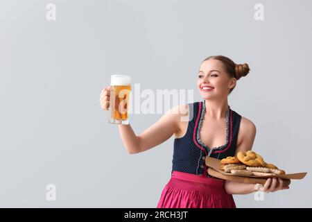 Wunderschöne Oktoberfest-Kellnerin mit Bier und Snacks auf hellem Hintergrund Stockfoto