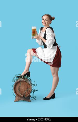 Wunderschöne Oktoberfest-Kellnerin mit Bier und Fass auf blauem Hintergrund Stockfoto