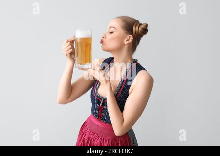 Wunderschöne Kellnerin auf dem Oktoberfest mit Bierkuss auf hellem Hintergrund Stockfoto