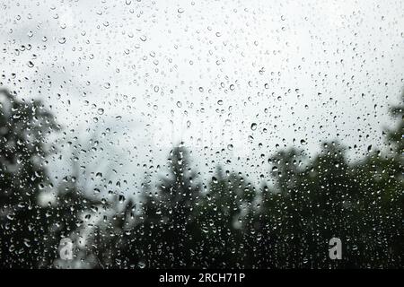 Eine Landschaft mit einem Anwesen am See, umgeben von Wäldern, die die Straße hinunter fahren, mit einem Regenbogen am Ende und Regentropfen auf der Fensterbank. Stockfoto