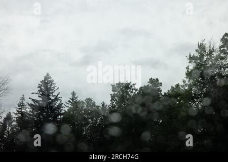 Eine Landschaft mit einem Anwesen am See, umgeben von Wäldern, die die Straße hinunter fahren, mit einem Regenbogen am Ende und Regentropfen auf der Fensterbank. Stockfoto