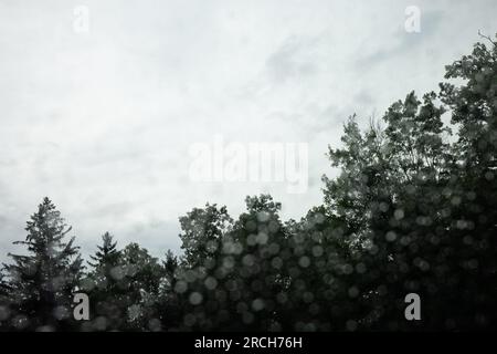 Eine Landschaft mit einem Anwesen am See, umgeben von Wäldern, die die Straße hinunter fahren, mit einem Regenbogen am Ende und Regentropfen auf der Fensterbank. Stockfoto