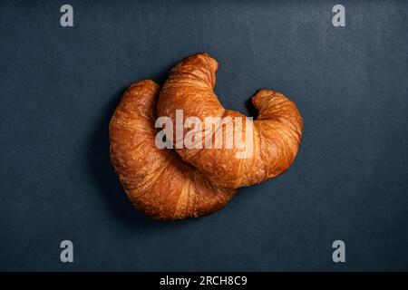 Zwei frische, leckere Croissants auf dunklem Hintergrund, Draufsicht Stockfoto