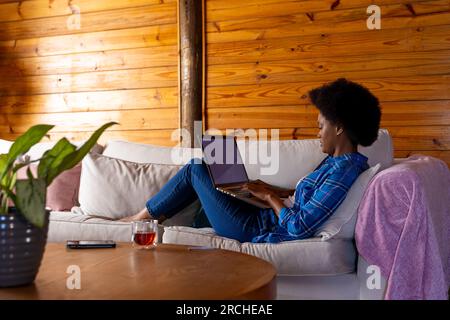 Eine afroamerikanische Frau, die sich auf dem Sofa mit einem Laptop zu Hause entspannt Stockfoto