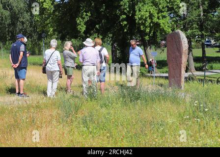 Mariefred, Schweden - 26. Juni 2023: Eine Gruppe von Touristen mit einem Reiseleiter hat sich vor einem Runenstein neben dem Schloss Gripsholm versammelt. Stockfoto