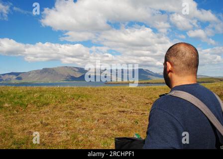 Ein Mann steht auf Videy Island, Island und schaut auf die Berge in der Ferne. Stockfoto