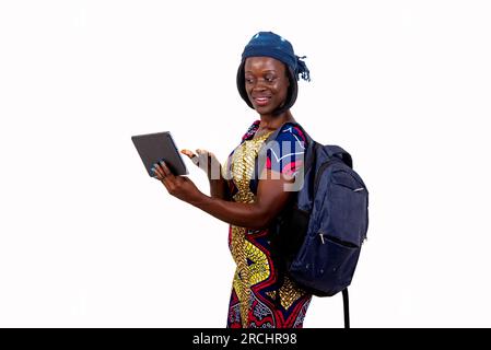 Porträt einer jungen Schülerin, die einen Rucksack trägt und mit einem lächelnden Tablet mit der Hand winkt. Stockfoto