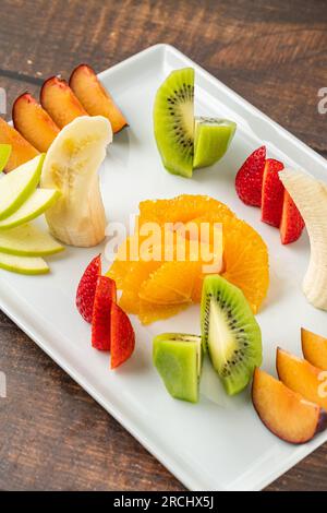 Gemischte Obstsorten auf weißem Porzellanteller auf Holztisch Stockfoto