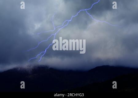 Blitze am dunklen Himmel mit Sturmwolken über den Bergen. Stockfoto