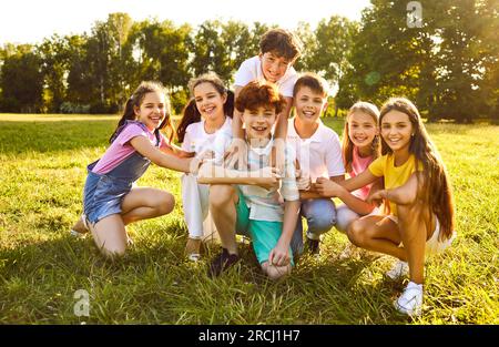 Glückliche Kinder sitzen im Freien auf dem Rasen und lächeln in den Sommerferien im Park. Stockfoto