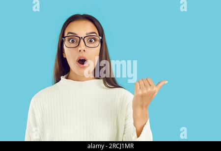 Witzig überrascht, dass eine junge Frau dich mit schockiertem Ausdruck ansieht, während sie auf den Kopierraum zeigt. Stockfoto