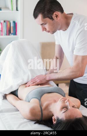Therapeut führt eine Sitzung mit lokalisierter Massage in der Bauchregion, um die Gesundheit des Patienten in Bezug auf die inneren Organe zu verbessern. Stockfoto