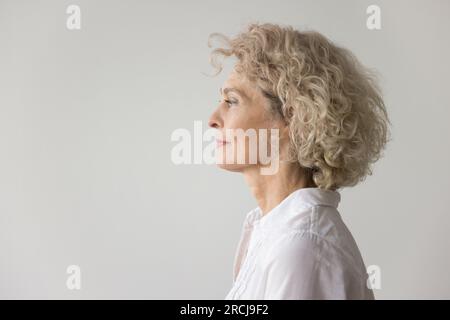 Eine durchdachte, sehr blonde, reife Frau, die auf weißem Hintergrund steht Stockfoto