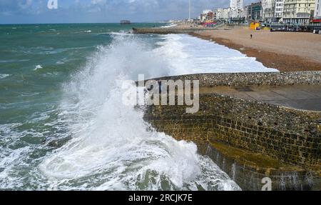 Brighton UK 15. Juli 2023 - Besucher werden nass, wenn sie sehen, wie riesige Wellen am Brighton Beach und am Ufer des Piers krachen, als ungewöhnlich starker Wind für Juli Batter Teile des Vereinigten Königreichs : Credit Simon Dack / Alamy Live News Stockfoto