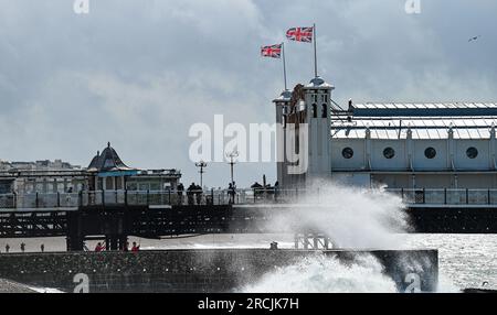 Brighton UK 15. Juli 2023 - Besucher werden nass, wenn sie sehen, wie riesige Wellen am Brighton Beach und am Ufer des Piers krachen, als ungewöhnlich starker Wind für Juli Batter Teile des Vereinigten Königreichs : Credit Simon Dack / Alamy Live News Stockfoto