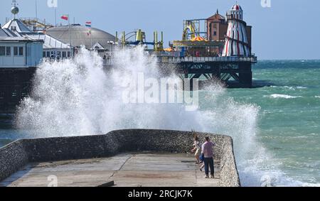 Brighton UK 15. Juli 2023 - Besucher werden nass, wenn sie sehen, wie riesige Wellen am Brighton Beach und am Ufer des Piers krachen, als ungewöhnlich starker Wind für Juli Batter Teile des Vereinigten Königreichs : Credit Simon Dack / Alamy Live News Stockfoto
