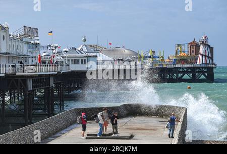 Brighton UK 15. Juli 2023 - Besucher werden nass, wenn sie sehen, wie riesige Wellen am Brighton Beach und am Ufer des Piers krachen, als ungewöhnlich starker Wind für Juli Batter Teile des Vereinigten Königreichs : Credit Simon Dack / Alamy Live News Stockfoto