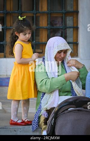 Türkische Frau mit Kind, die auf den Stufen der Blauen Moschee in Istanbul, Türkei, sitzt Stockfoto